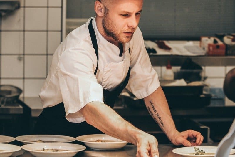 Male Chef in kitchen pushing a plate along table