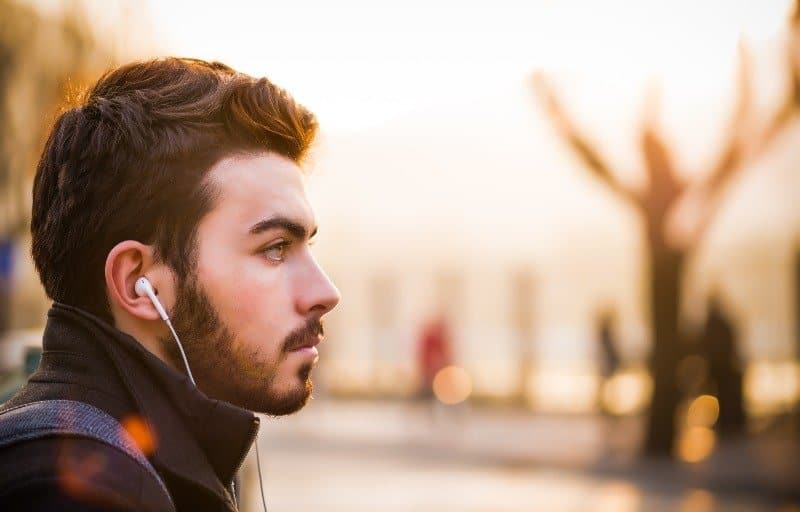 Man wearing headphones staring out at sunrise | Why Listening to Music is Invaluable Shift Work Sleep Advice