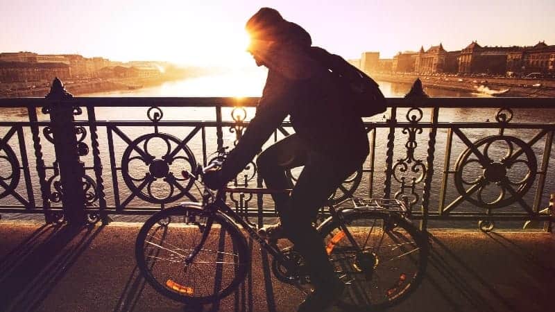 Man riding bike with sun over bridge | Is working night shift unhealthy for you